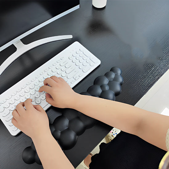 Personne tapant sur un clavier avec un repose-poignet noir en forme de nuage sur un bureau noir.