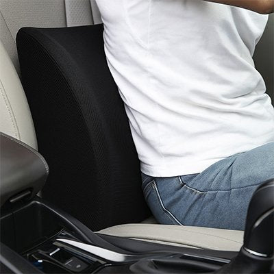 Conducteur utilisant un coussin de soutien lombaire noir sur un siège de voiture pour soulager les douleurs du bas du dos pendant la conduite.