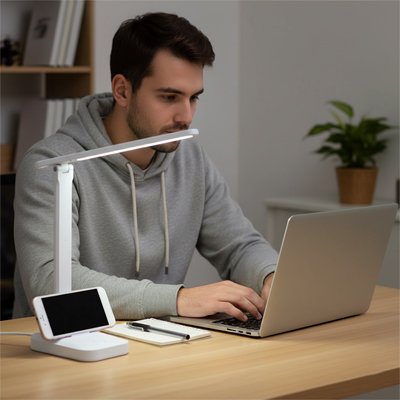Homme travaillant sur un bureau moderne éclairé par une lampe LED blanche équipée d’un support pour téléphone.