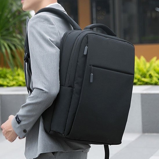 Homme portant un sac à dos ordinateur noir élégant, sac ergonomique avec compartiments adaptés pour télétravail, bureau et voyages d’affaires.