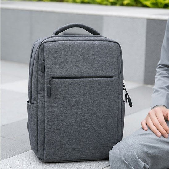 Homme en costume portant un sac à dos ordinateur gris foncé, sac business élégant et ergonomique pour travail et déplacements professionnels.