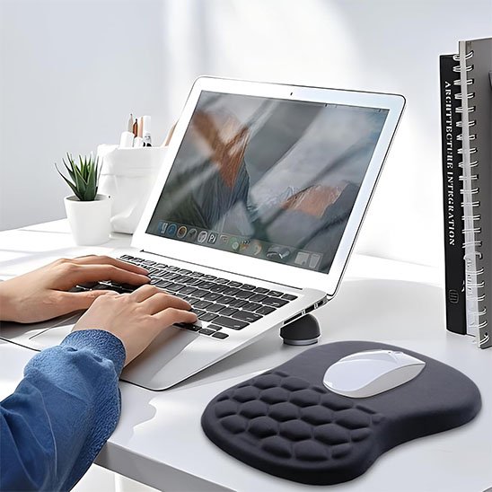 Utilisateur travaillant sur ordinateur portable avec tapis de souris ergonomique noir en gel alvéolé offrant un soutien optimal du poignet.