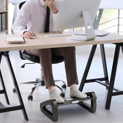 Homme assis à son bureau, les pieds posés sur un repose-pieds ergonomique incliné