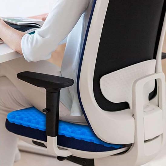 Femme assise sur un coussin en gel bleu alvéolé posé sur une chaise de bureau, pour soulager le dos et améliorer la posture en télétravail.