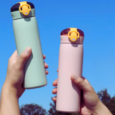 Deux gourdes isothermes 460 ml rose et vert menthe tenues à la main en extérieur sous un ciel bleu.