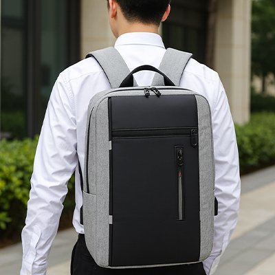 Homme vêtu d’une chemise blanche portant un sac à dos ordinateur gris et noir, idéal pour les trajets domicile-travail et les rendez-vous professionnels.