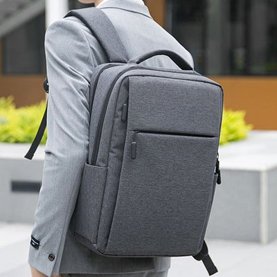 Homme en costume portant un sac à dos ordinateur gris foncé, sac business élégant et ergonomique pour travail et déplacements professionnels.
