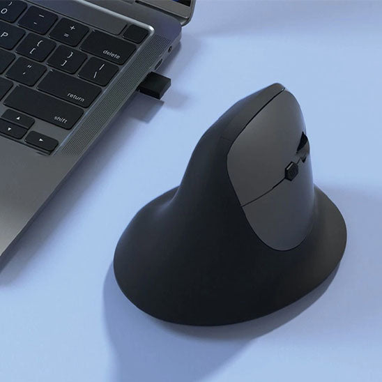 Souris ergonomique posée à côté d’un ordinateur portable, connectée via port USB.

