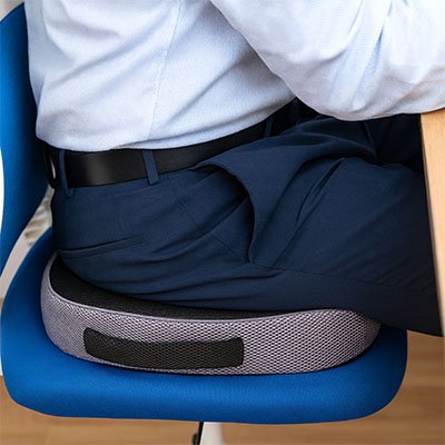 Vue arrière d’un homme assis sur un coussin ergonomique respirant, démontrant le maintien du coccyx et la posture droite.