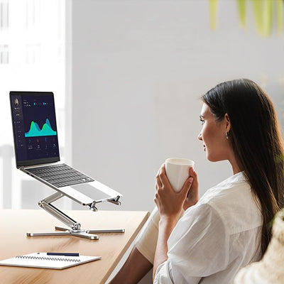 Femme travaillant depuis chez elle avec un support ordinateur portable pliable en aluminium argenté, profitant d’une posture saine et d’un confort visuel.