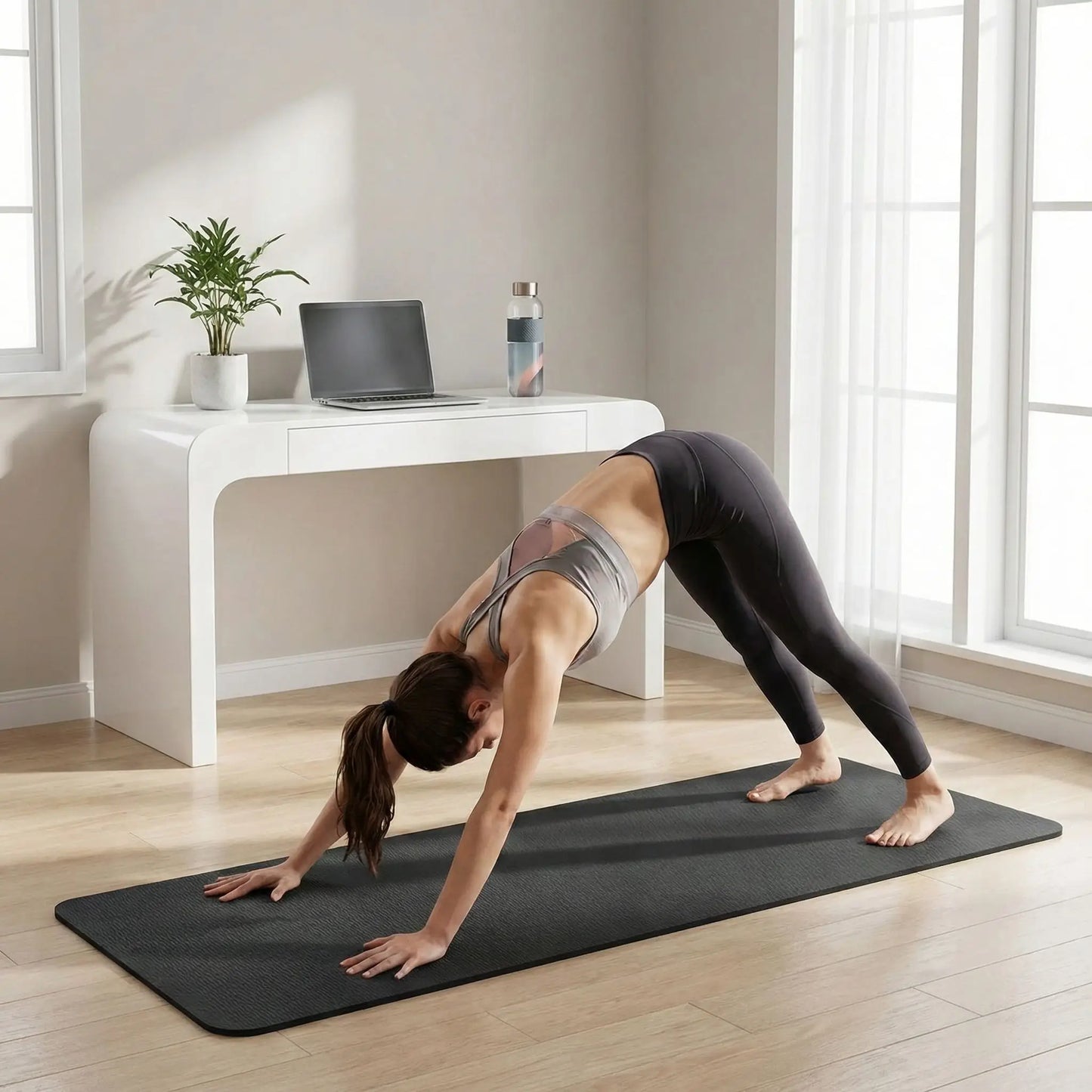 Femme pratiquant le yoga en posture chien tête en bas sur tapis noir antidérapant 6 mm dans un espace de télétravail