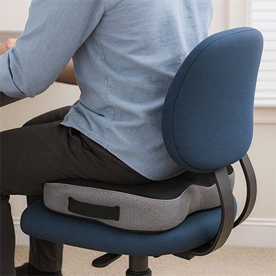 Homme assis sur un coussin ergonomique sur une chaise de bureau, montrant la position correcte du dos et du coccyx.